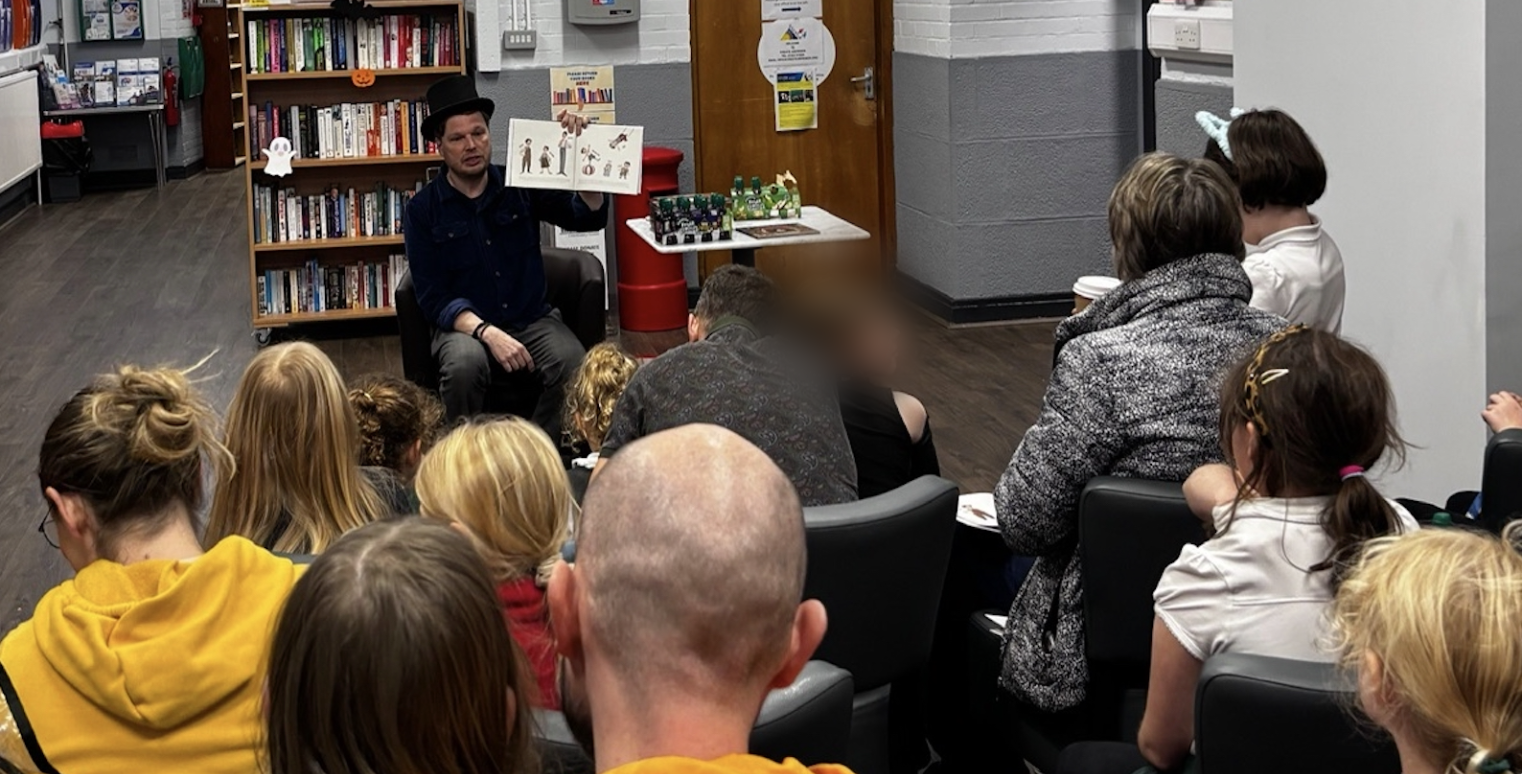 Aldo de Pape in a top hat reading The Magical Manacles to a full room of families