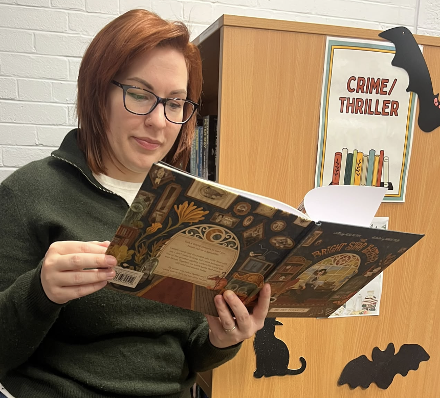 A guest reading The Tiny Typewriter by the Halloween bookshelves