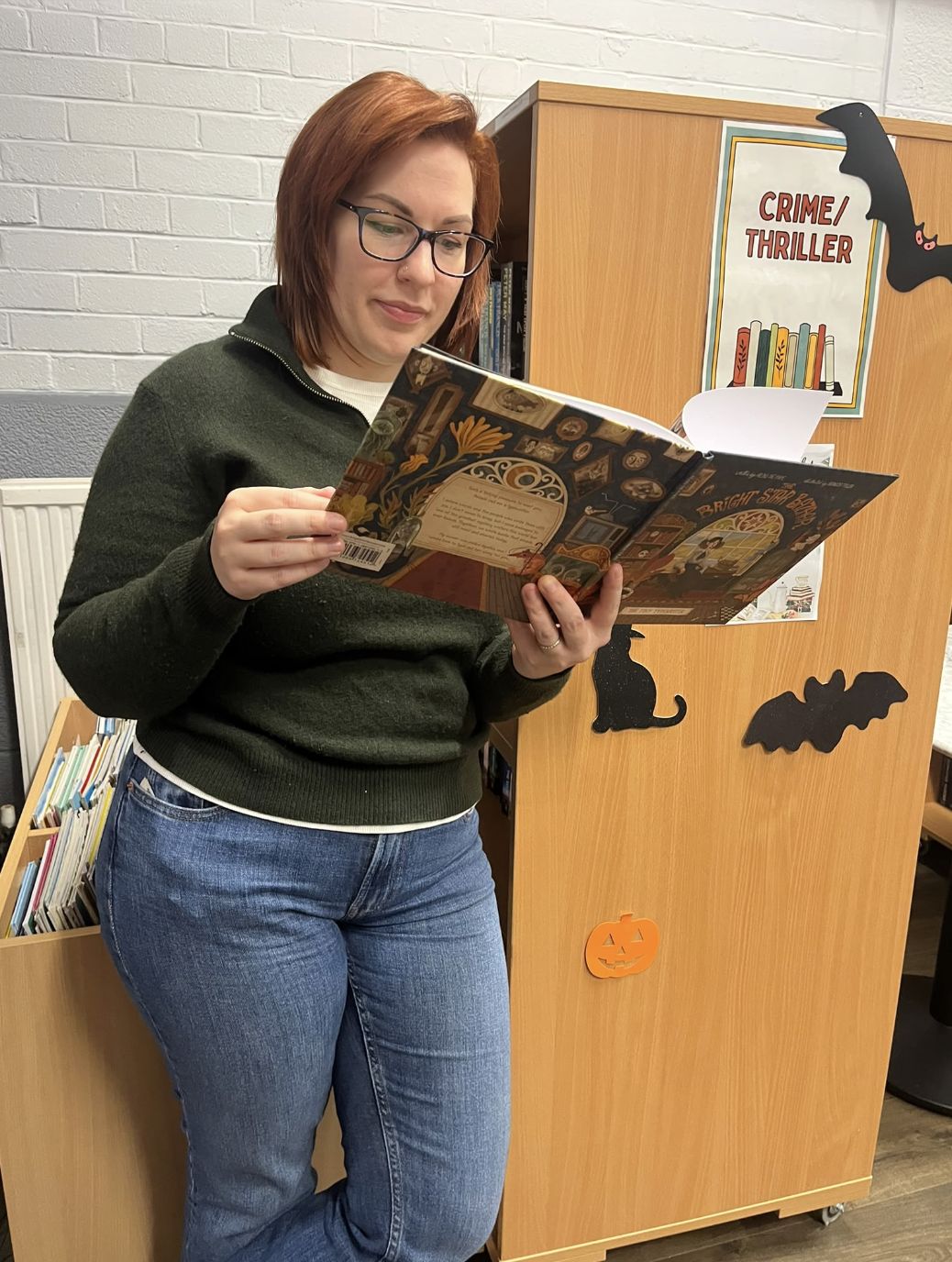 A guest reading The Tiny Typewriter by the Halloween bookshelves